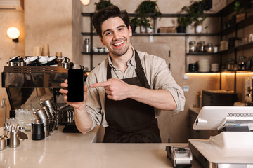 Happy coffee man posing in cafe bar working indoors showing display of mobile phone.