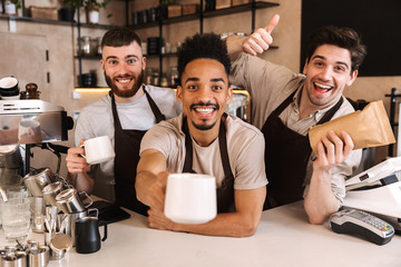 Group of cheerful men baristas wearing aprons