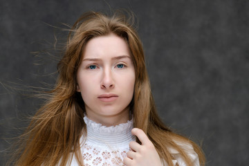 Naklejka premium Close-up portrait of a young pretty brunette girl woman with beautiful long hair on a gray background in a white jacket. He talks, smiles, shows his hands with emotions in various poses.