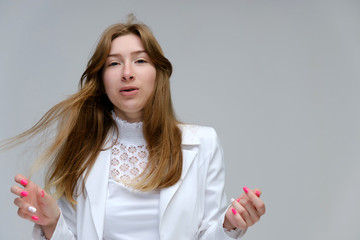 Portrait to the waist of a young pretty brunette girl woman with beautiful long hair on a white background in a white jacket. He talks, smiles, shows his hands with emotions in various poses.