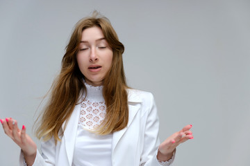 Portrait to the waist of a young pretty brunette girl woman with beautiful long hair on a white background in a white jacket. He talks, smiles, shows his hands with emotions in various poses.