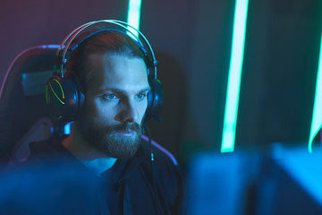Concentrated zombie gamer with beard wearing headset sitting in front of computer monitor in dark video game club © Seventyfour