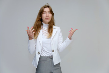Portrait to the waist of a young pretty brunette girl woman with beautiful long hair on a white background in a white jacket and gray pants. Talks, smiles, shows hands with emotions in various poses.