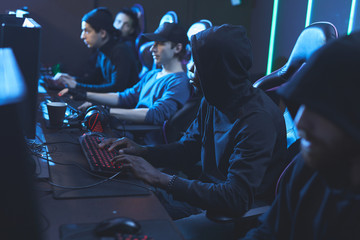 Group of concentrated young software developers in dark outfits sitting in row and working in...