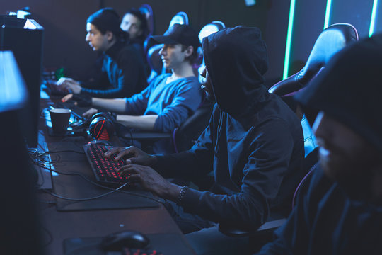 Group of concentrated young software developers in dark outfits sitting in row and working in server center