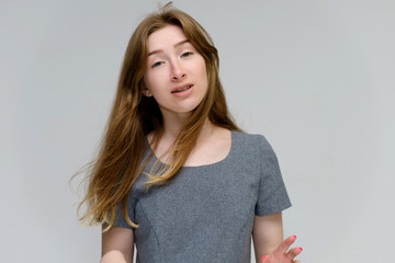 Portrait below the chest of a young pretty brunette girl woman with beautiful long hair on a white background in a gray dress. He talks, smiles, shows his hands with emotions in various poses.