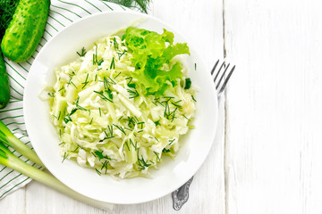 Salad of cabbage with cucumber in plate on board top