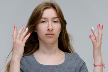 Obraz premium Close-up portrait of a young pretty brunette girl woman with beautiful long hair on a white background in a gray dress. He talks, smiles, shows his hands with emotions in various poses.