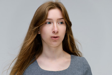 Naklejka premium Close-up portrait of a young pretty brunette girl woman with beautiful long hair on a white background in a gray dress. He talks, smiles, shows his hands with emotions in various poses.