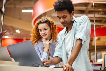 African guy with a red-haired girl in an electronics store choosing a laptop to buy on credit