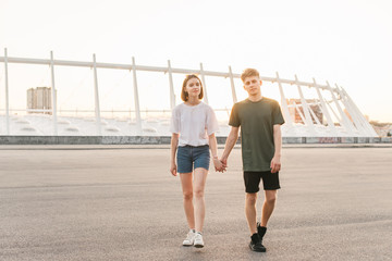 Beautiful lovely couple strolls by holding hands in the background of the city landscape,looking into the camera and smiling.Portrait stylish couple of casual clothes in the background of the city