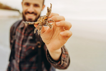 Portrait of a stylish bearded man with a small crab in his hands during the first tour of the sea