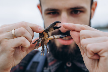 A cool picture of a man who holds a small crab in his arms while walking along the sea in cloudy cold weather