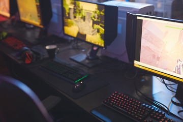 Close-up of computer monitors with arcade game pictures place on table with colorful keyboards in video game club