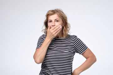 Surprised mature woman covering mouth with hand and staring at camera