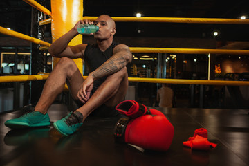Selective focus on boxing gloves, male African boxer drinking water on the background