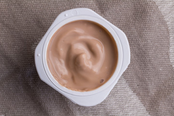 Yogurt cup with chocolate yoghurt on brown linen background