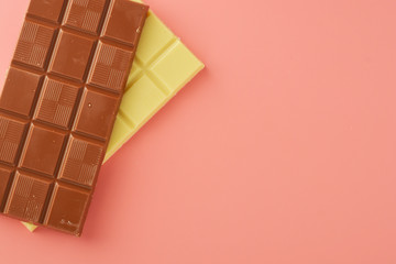 White and black chocolate bars over pink background, copy space.