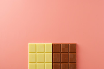 White and black chocolate bars over pink background, copy space.