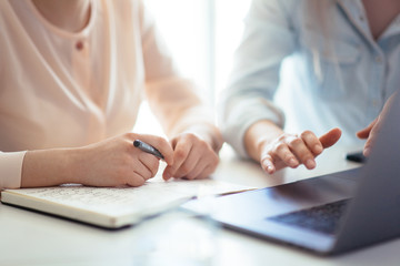 Girls dressed in casual discuss work issues, hands on a laptop