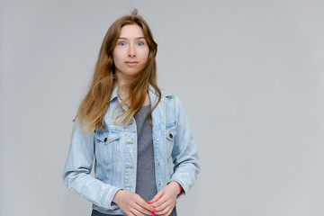 Portrait to waist of a young pretty brunette girl woman with beautiful long hair on a white background in a jacket from jeans. He talks, smiles, shows his hands with emotions in various poses.
