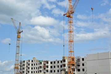 Construction of prefabricated houses. Two cranes and a house against a blue cloudy sky. Construction. Summer