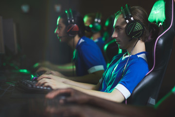 Group of concentrated video game club participants in modern headsets sitting in row and playing computer game © Seventyfour