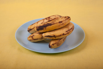 Ugly bananas lie on a blue plate on a yellow background . Copy spaes