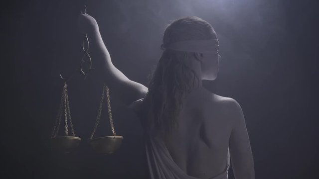 Ancient greek goddess Themis is standing in low lighting with the scales in hand