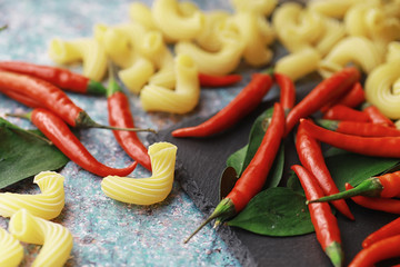 Uncooked pasta on a stone background. With seasonings and spices, spicy chili peppers.