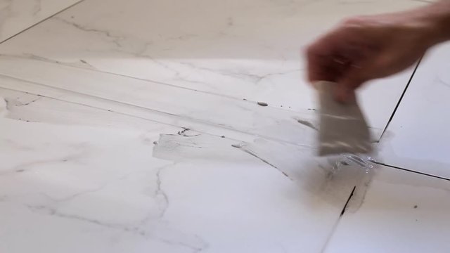 Grouting tiles seams with a rubber trowel