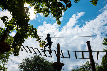 Young boy walking on a rope trail framed by green foliage with cloudy blue sky in the background