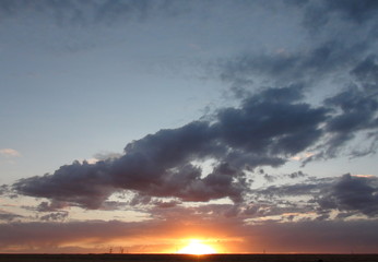 The natural picture of the combination of rainbow colors in the cloudy evening sky under the rays of the sun that sits behind the horizon.