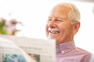 Senior is laughing and reading the newspaper outside in his garden