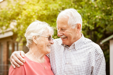 Smart older couple are standing in the garden, hugging each other and laughing at each other