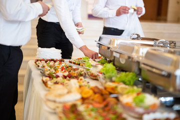Buffet table with food and waiters checking if everything is served correctly.