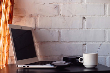 Desk with a white laptop, helmets, a cup of coffee and a mobile.