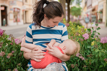 young brunete mother breast feeding baby girl outdoors in public town 