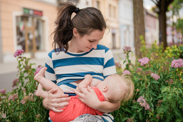 young brunete mother breast feeding baby girl outdoors in public town 