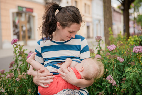 young brunete mother breast feeding baby girl outdoors in public town 