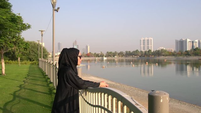 Muslim Arabic woman stares at the water on Barsha park in Dubai,UAE.