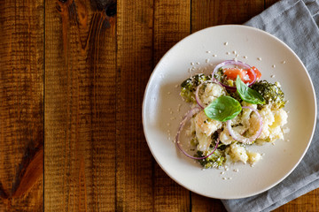 Vegetarian salad of broccoli, cauliflower, tomatoes, onions, Basil and sesame on a beautiful plate that stands on a wooden background