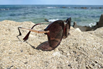 Closeup of female sunglasses on the rock near the sea. Brown sunglasses placed on rocks and sea background