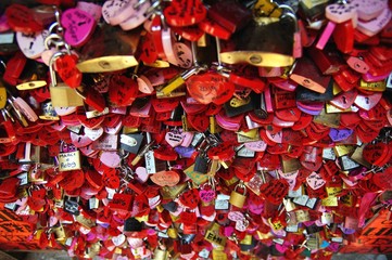 Fototapeta na wymiar Locked locks of love and loyalty. Wall full of red and pink love locks shaped as hearts and classical locks with writings on each lock,