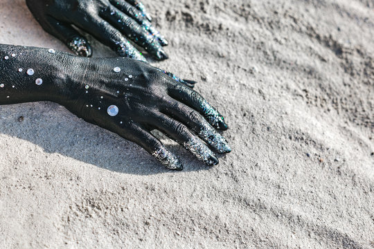 close up of woman hands painted black on sand. moon and stars concept