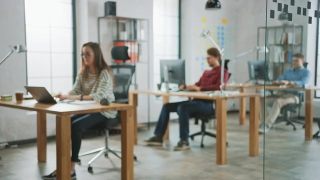 Blurred Footage of Creative Agency Life. Female Colleague Works with two Male Coworker Behind Desks. Creative Office Concept. They Work on Computers and Laptops.