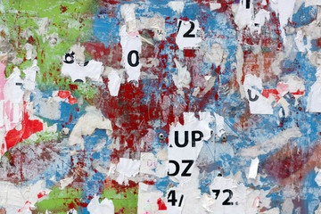 Grungy flat wall surface covered with pealed paper and red, green and blue spray paint 