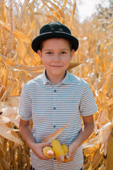 Little caucasian boy on the corn farm. Harvest season. Happy smiling little boy with dry corn.