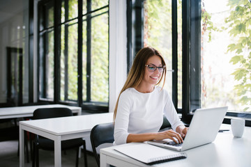 Beautiful young woman using laptop in modern co-working space.