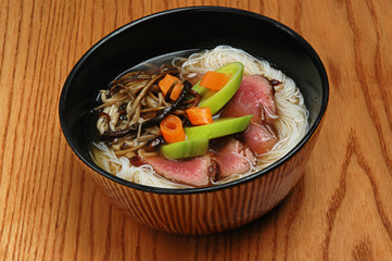 Japanese food udon with noodles and meat in a dark bowl on a wooden background